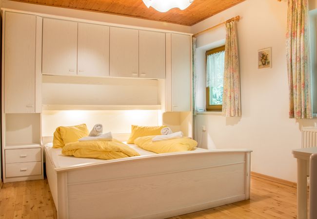 Helles, gemütliches Schlafzimmer mit hellem Holz, gelber Bettwäsche und zwei Fenstern.