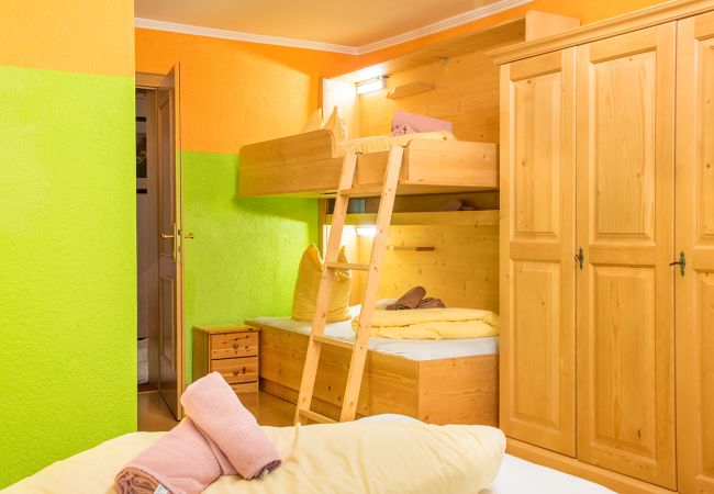 Buntes Kinderzimmer mit Etagenbett, Holzkleiderschrank und leuchtend grünen Wänden – freundlich und einladend.
